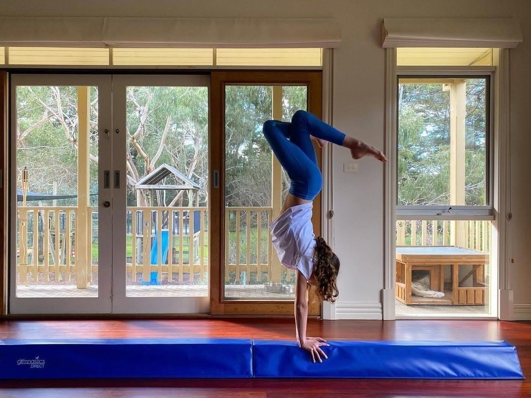 Young gymnast doing a handstand on a blue foam balance beam at home